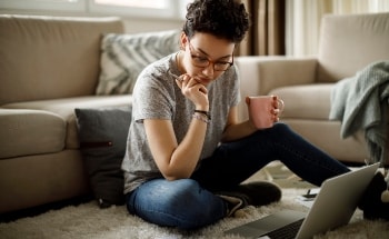 A women sitting on the floor of her living room looking at her laptop